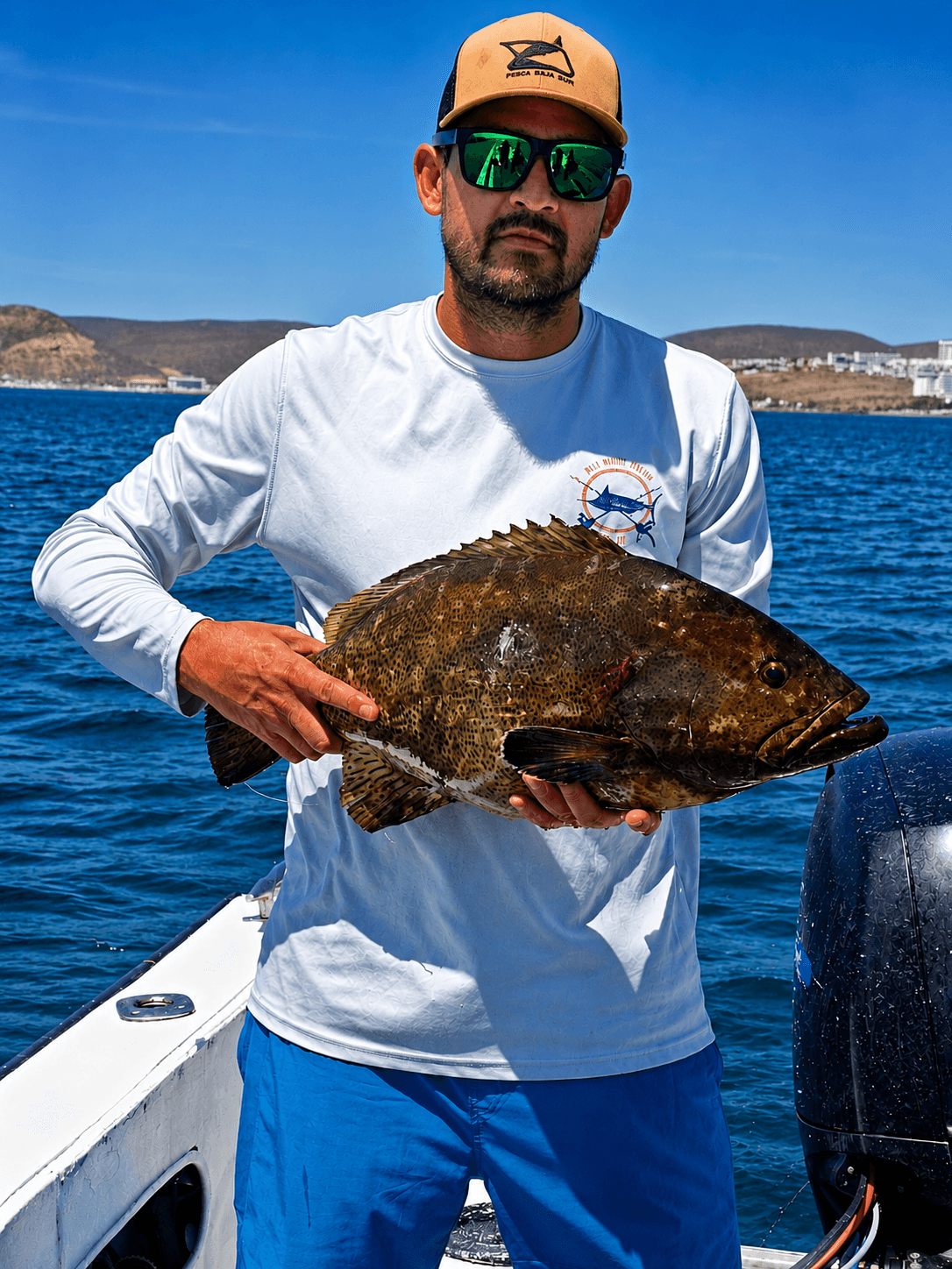 Captain holding a freshly caught grouper, with La Paz in the background